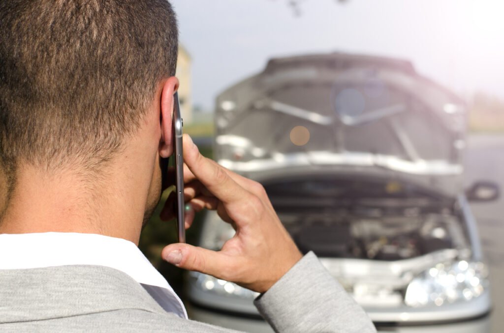 Conductor llamando por telu00e9fono junto a su coche tras un accidente de tru00e1fico